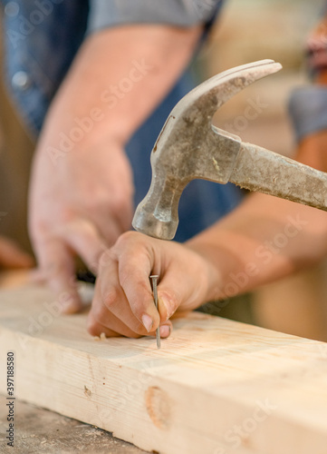 Close up father teaches son to hammer nails in the workshop