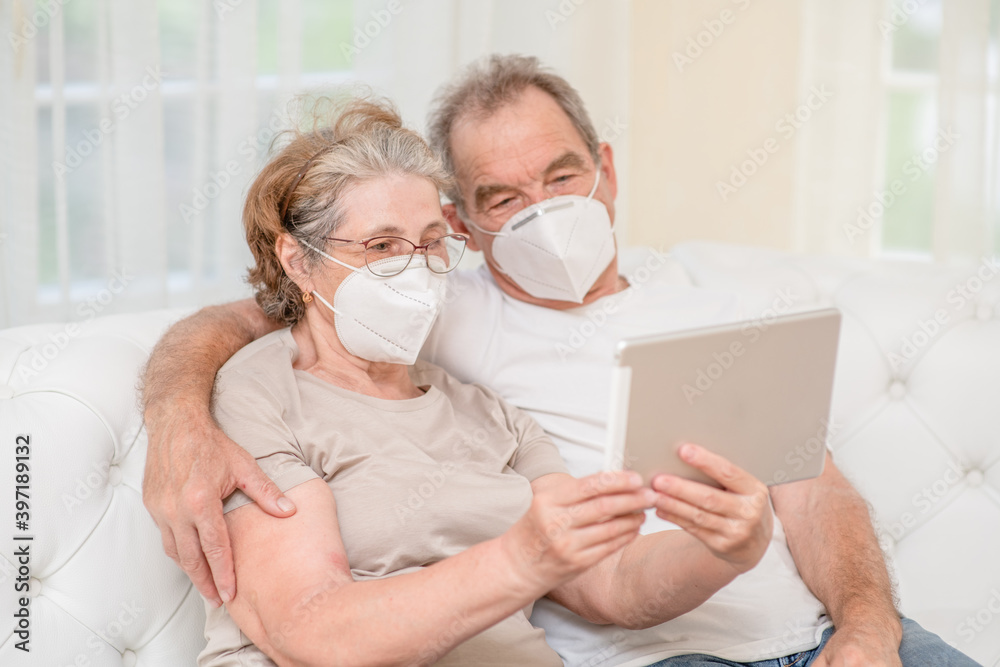 Happy senior couple wearing protective masks having video chat on tablet computer during the coronavirus epidemic