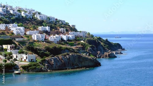 White Aegean houses of Gumusluk next to sea and moving yachts at sunny day in Bodrum, Turkey. Bodrum is most popular summer vacation area for tourist in Turkey. 