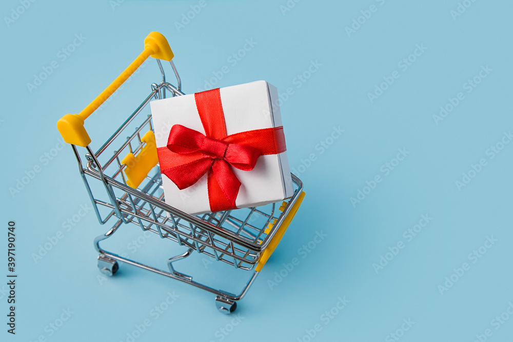 Shopping Cart with big gift box on blue background. Online Shopping Concept. Christmas Sales or gift shopping. Preparing for the New Year and Christmas. Buying gifts.