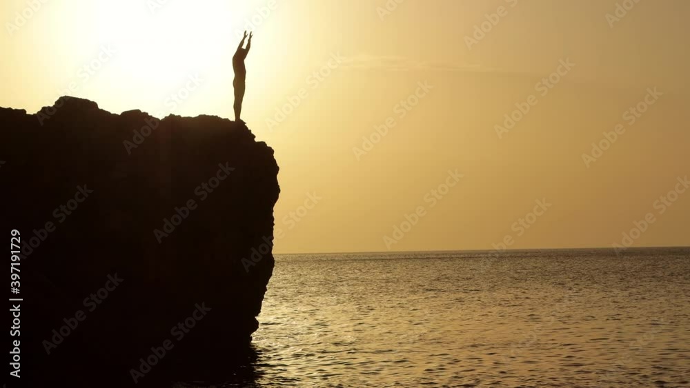 Silhouette of a man performing somersault from the cliff into the ocean