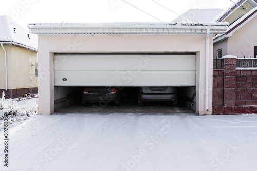 xterior of a  garage attached to a house. garage with two cars inside in winter. semi-open sectional  doors