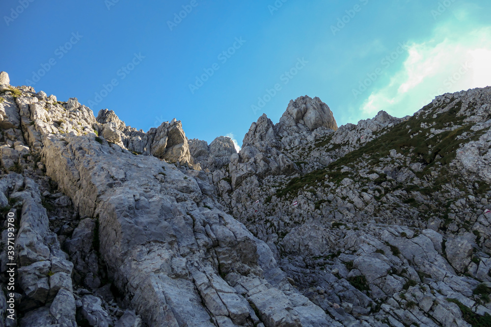 A steep mountain wall on the way to Grimming in Austrian Alps. Dangerous climbing only for professionals. The sky above it is blue, one small cloud. Extreme sport. red path mark on the side.