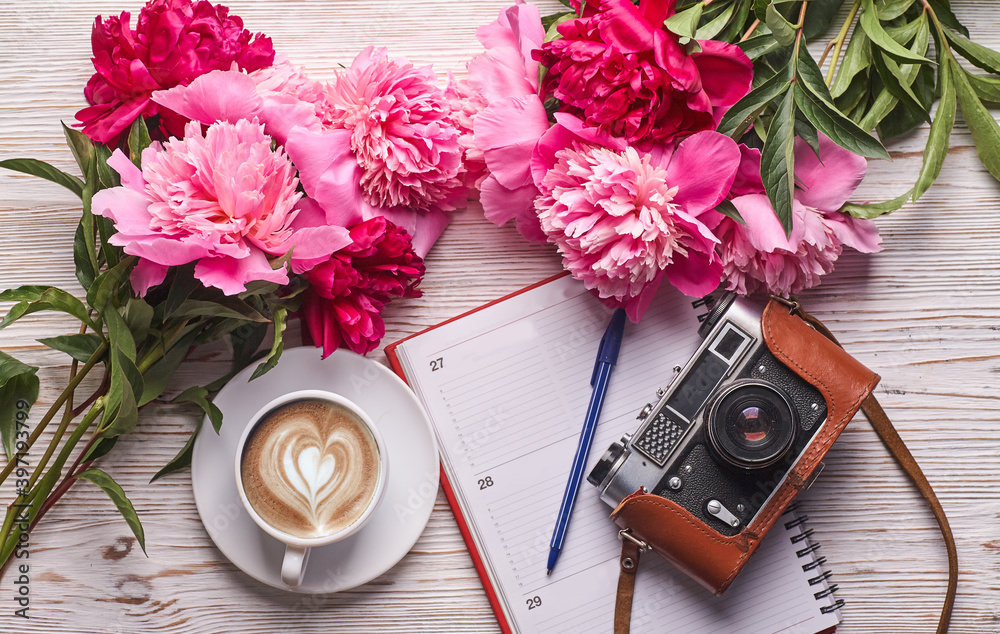 Flat lay women's office desk. Female workspace with laptop, pink peonies bouquet, camera and coffee on white background. Top view feminine background.