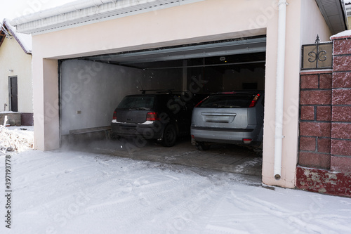 xterior of a  garage attached to a house. garage with two cars inside in winter. semi-open sectional  doors