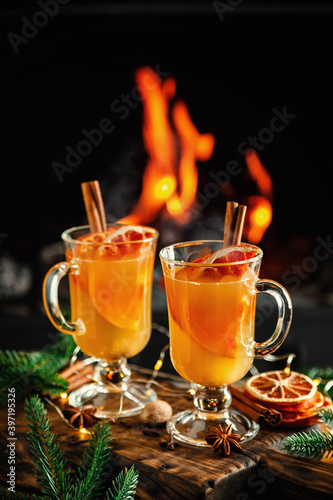 Mulled cider glasses on the background of fireplace fire. Hot mulled spiced apple cider cocktail for winter or autumn time.