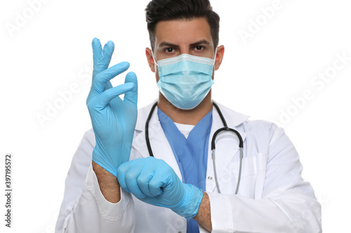 Doctor in protective mask putting on medical gloves against white background