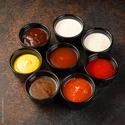 Set of sauces - ketchup, mayonnaise, mustard soy sauce, bbq sauce, pesto, mustard grains and pomegranate sauce on dark rusty stone or metal background.