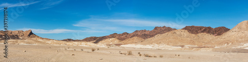 a wide panorama of the outside of the south rim of the makhtesh ramon crater in israel including the israel national trail on ramon's tooth magmatic intrustion with wispy clouds in the background