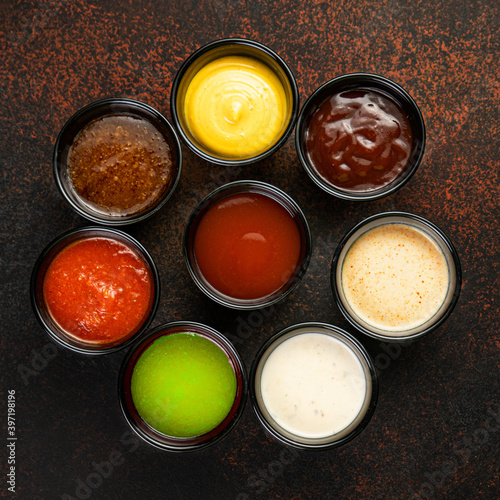 Set of sauces - ketchup, mayonnaise, mustard soy sauce, bbq sauce, pesto, mustard grains and pomegranate sauce on dark rusty stone or metal background.