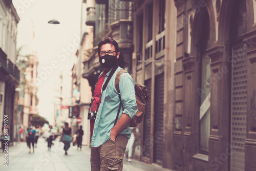 Tourist and tourism season in coroanvirus covid-19 emergeny restrictions - adult man standing outdoors on the street in the city wearing protection face medical black mask to prevent contagion