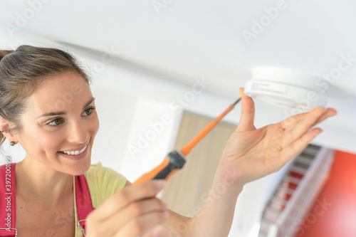 Young woman is fitting a fire alarm in the ceiling