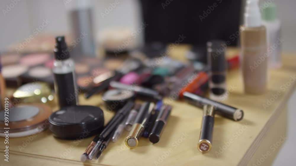 Close up shot of hand of unrecognizable make-up artist taking mascara of lipstick from table with various cosmetic products Close up shot of hand of unrecognizable make-up artist taking mascara of lipstick from table with various cosmetic products