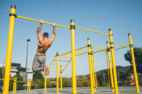 Young athletic man doing gymnastics on bars at a calisthenics park photo
