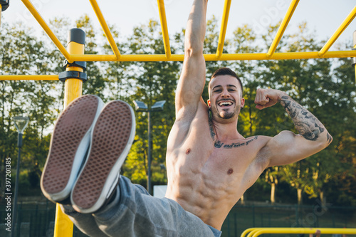 Funny athletic young man hanging from the bars showing his muscles