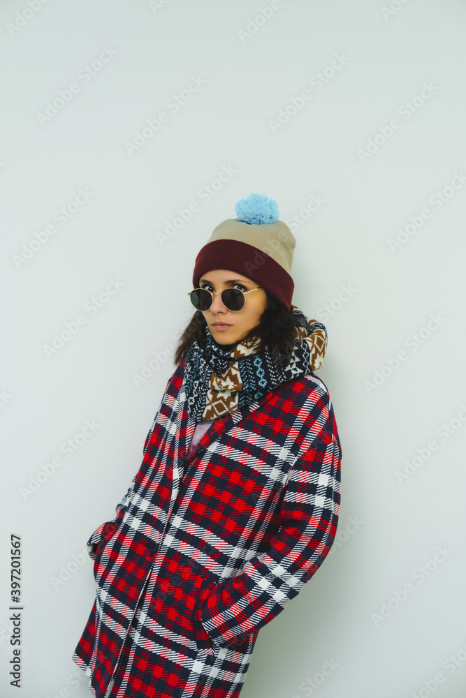 Beautiful pretty fashion model in trendy urban street outfit. Stylish posing. Sunglasses, red coat, scarf and funny beanie.