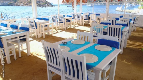Traditional Aegean fish restaurant, tables and chairs next to see in Gumusluk Town, Bodrum, Turkey at sunny day. Bodrum is very popular and famous place for tourist.