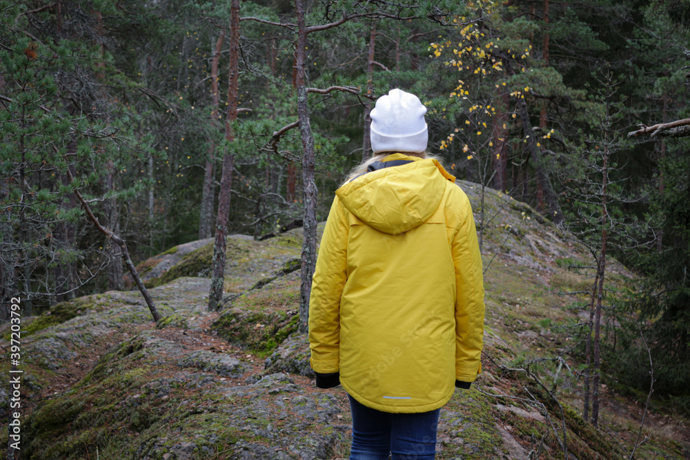 European young woman in a yellow jacket on a rock in the deep northern forest