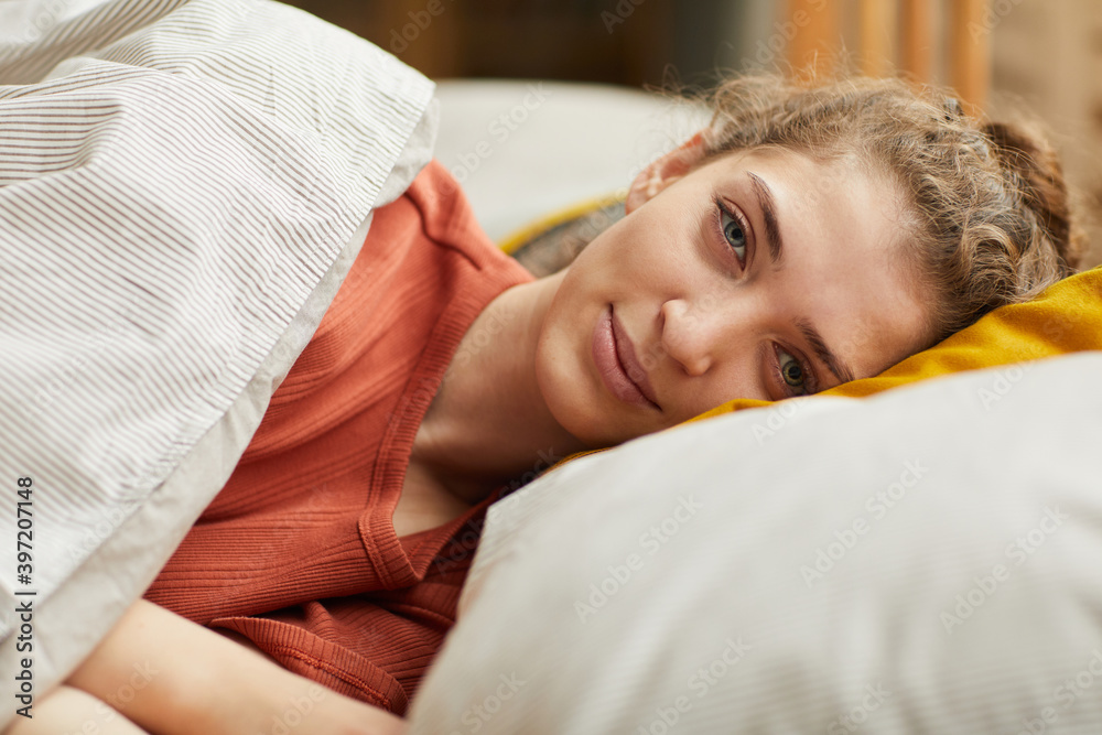 Fototapeta premium Portrait of young woman lying on pillow looking at camera while resting in her bed at home
