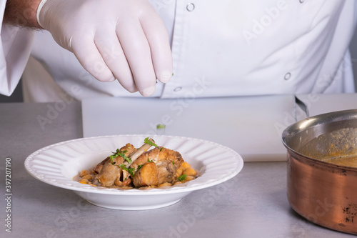 view of male chef hand sprinkling chopped parsley on a plate with chickpea stew and meat
