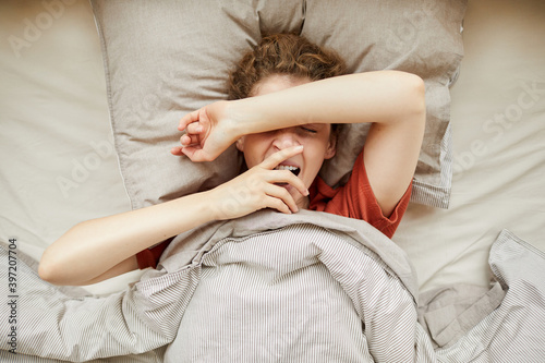 High angle view of young woman lying in her bed and yawning waking up in the morning