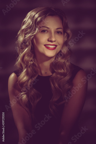 Beautiful smiling model with wavy hairstyle posing in black dress. image toned in warm colors in retro style
