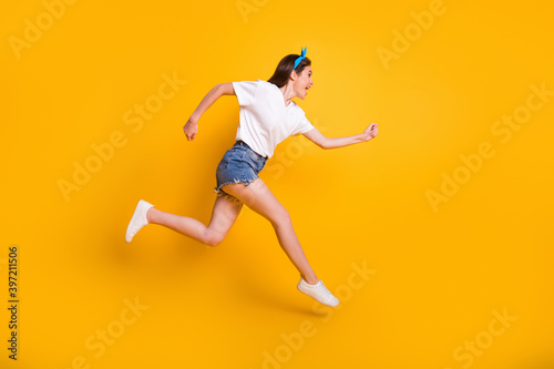 Full length body size side profile photo of girl running fast jumping high yelling isolated on vibrant yellow color background