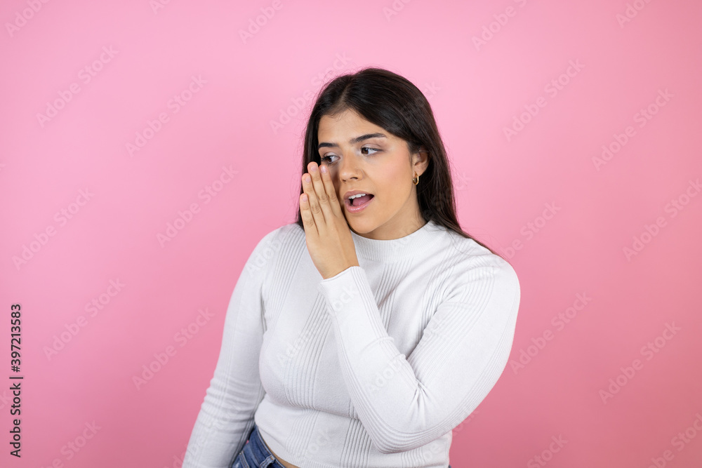 Young beautiful woman over isolated pink background hand on mouth telling secret rumor, whispering malicious talk conversation
