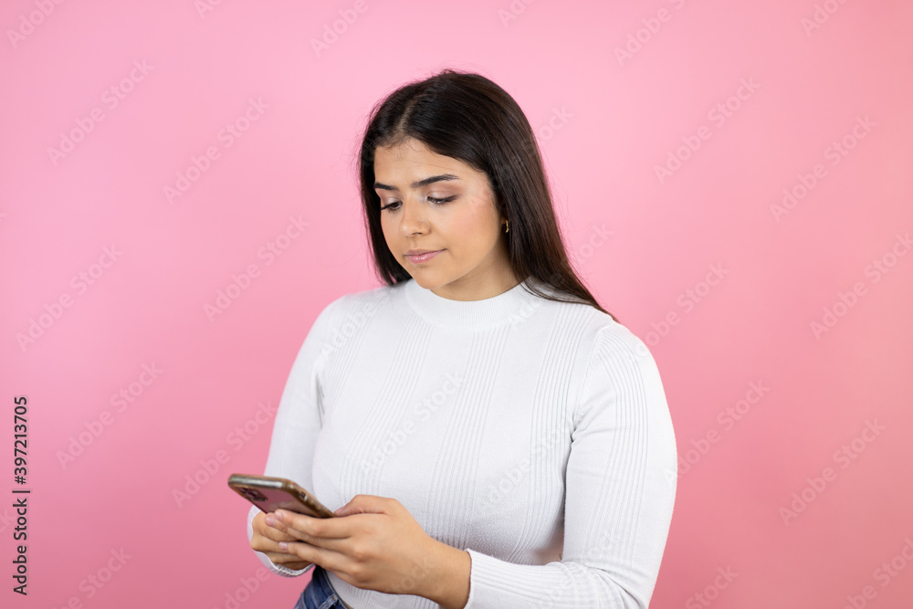Young beautiful woman over isolated pink background texting with her phone