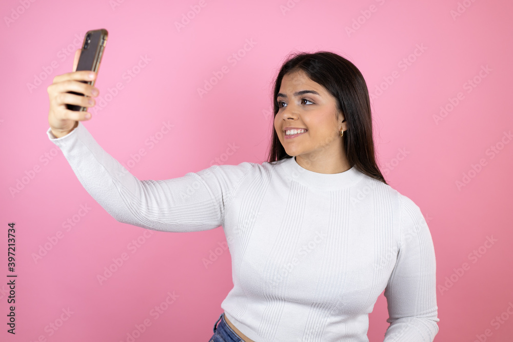 Young beautiful woman over isolated pink background taking a selfie with her phone Young beautiful woman over isolated pink background taking a selfie with her phone