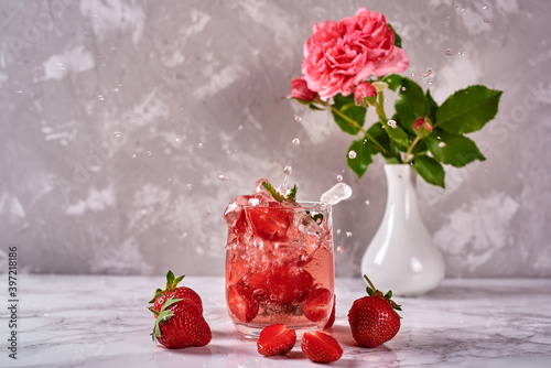 Fresh strawberry lemonade in sparkling glasses and rose in vase on gray table background, copy space. Cold summer drink. Berry cocktail. Splash