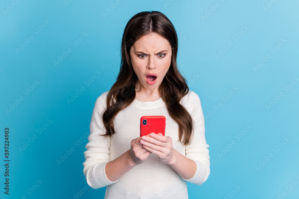 Photo of angry impressed wavy lady wear white sweater holding looking modern device isolated blue color background Photo of angry impressed wavy lady wear white sweater holding looking modern device isolated blue color background