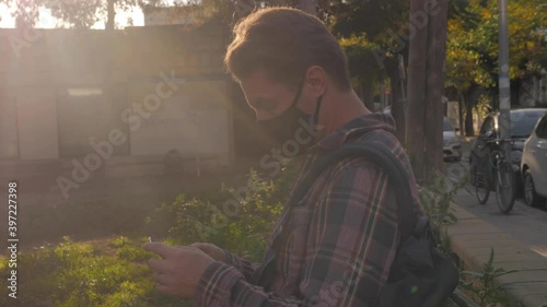 Adult man with surgical medical mask sitting on a bench and using phone, businessman in park relax, safe travel