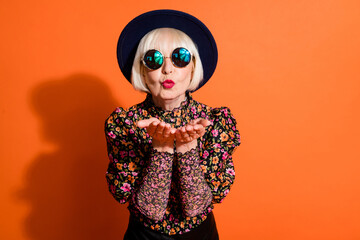 Portrait of cool beautiful hipster grandmother send air kiss camera with red lipstick isolated on orange color background