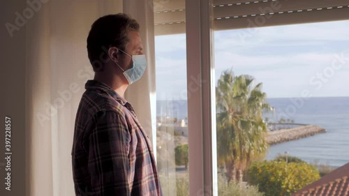 Middle aged man on the balcony of the house during the covid-19 outbreak lockdown. male with medical mask, worried and tired face looking at the street depressed in quarantine. Isolation concept