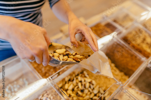 Unrecognizable girl put nuts in paper bag Customer buying groceries in zero waste shop or local home bakery. Buying foods without plastic packaging.