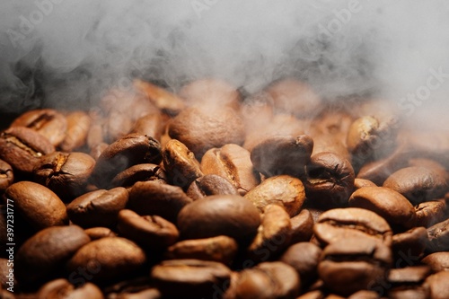 Macro view of freshly roasted fresh Arabica coffee beans with smoke, extreme close up photo of fresh and steamy coffee beans on dark background.