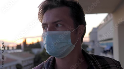 man hotel guest wearing protective mask to protect from coronavirus, male on balcony with sea view