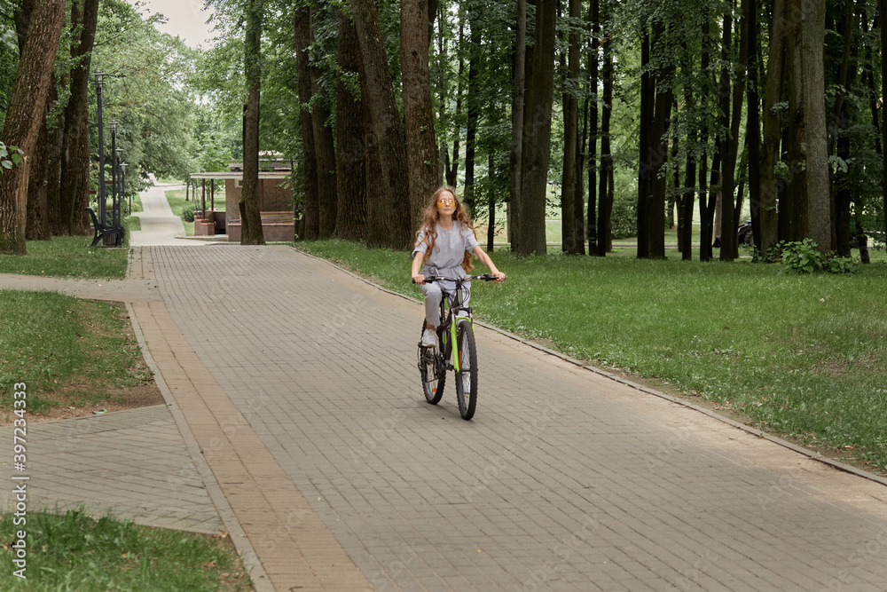 Beautiful girl in sunglasses with long hair rides a Bicycle. Playing sports during the pandemic. Outdoor activity.