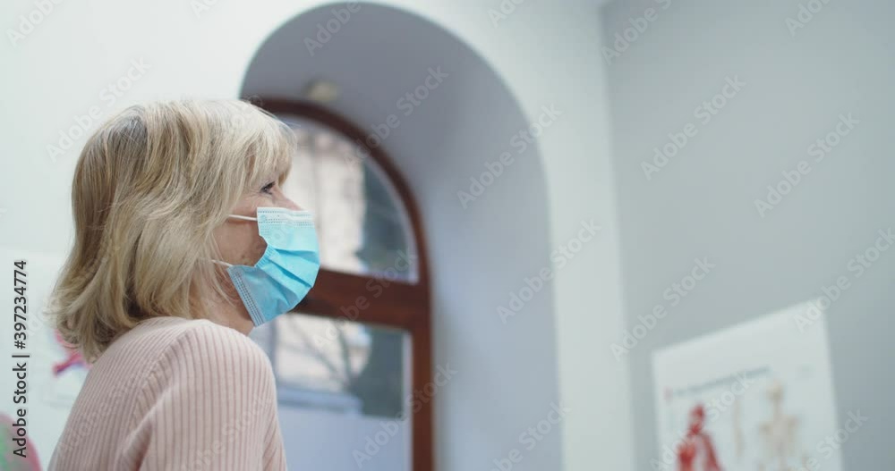 Close up portrait of Caucasian handsome male professional doctor in medical mask examining senior woman patient at consultation in hospital. Coronavirus pandemic. Covid-19 concept