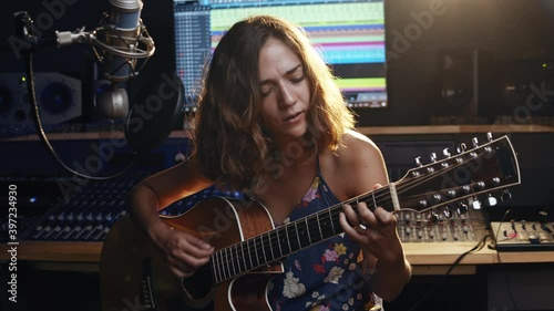 Music studio. Creative world. Musician. Latin woman playing guitar and singing in the recording studio. An attractive brunette female person in a beautiful shirt records songs. 