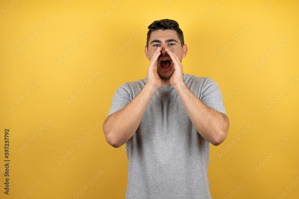 Young handsome man wearing a casual t-shirt over isolated yellow background shouting and screaming loud to side with hands on mouth Young handsome man wearing a casual t-shirt over isolated yellow background shouting and screaming loud to side with hands on mouth