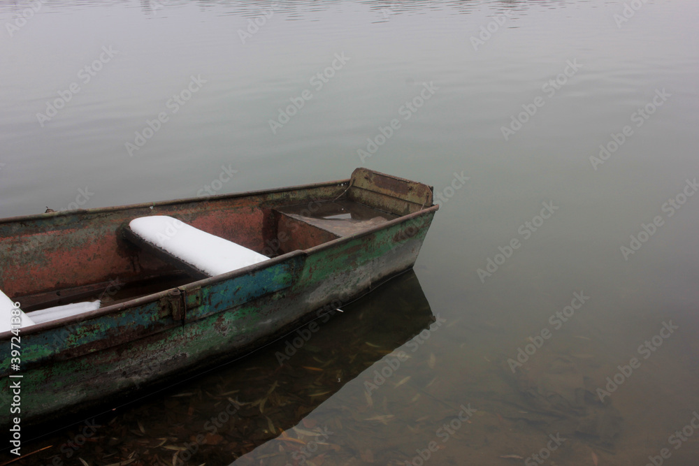 Old shabby boat covered with snow on the winter river