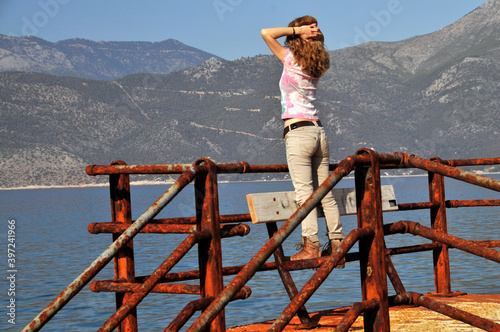 Woman enjoying the fresh air and standing on rusty railings by the sea