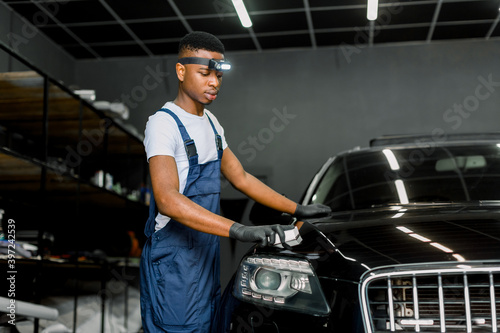 African male auto service worker, coating luxury black car with professional nanoceramic composition for car body care and to protect from scratches, chips and damage. © sofiko14