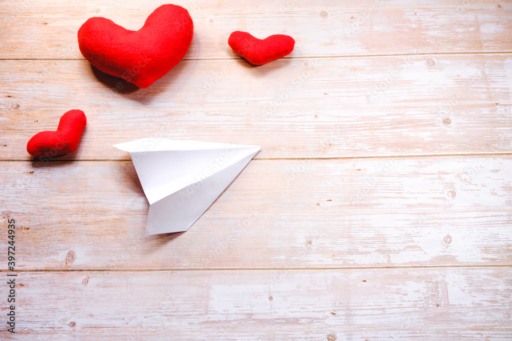 DIY for Valentines day. Instructions step by step. Do it yourself at home. Paper airplane the art of origami. White paper airplane on wooden table next to three red toy hearts. Step 7.