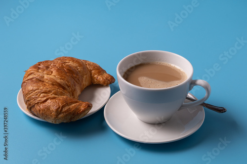 Cup of milk coffee and croissant on blue background  copy space for text
