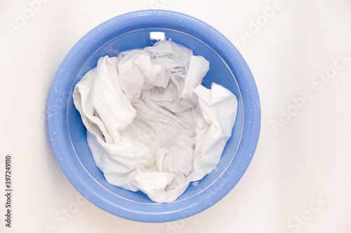 Laundry concept with Soak white clothes in blue bowl prepared for hand washing with copy space on white background