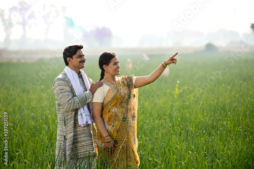 Happy Indian couple farmers examining crop in agricultural field