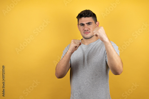 Young handsome man wearing a casual t-shirt over isolated yellow background Punching fist to fight, aggressive and angry attack, threat and violence